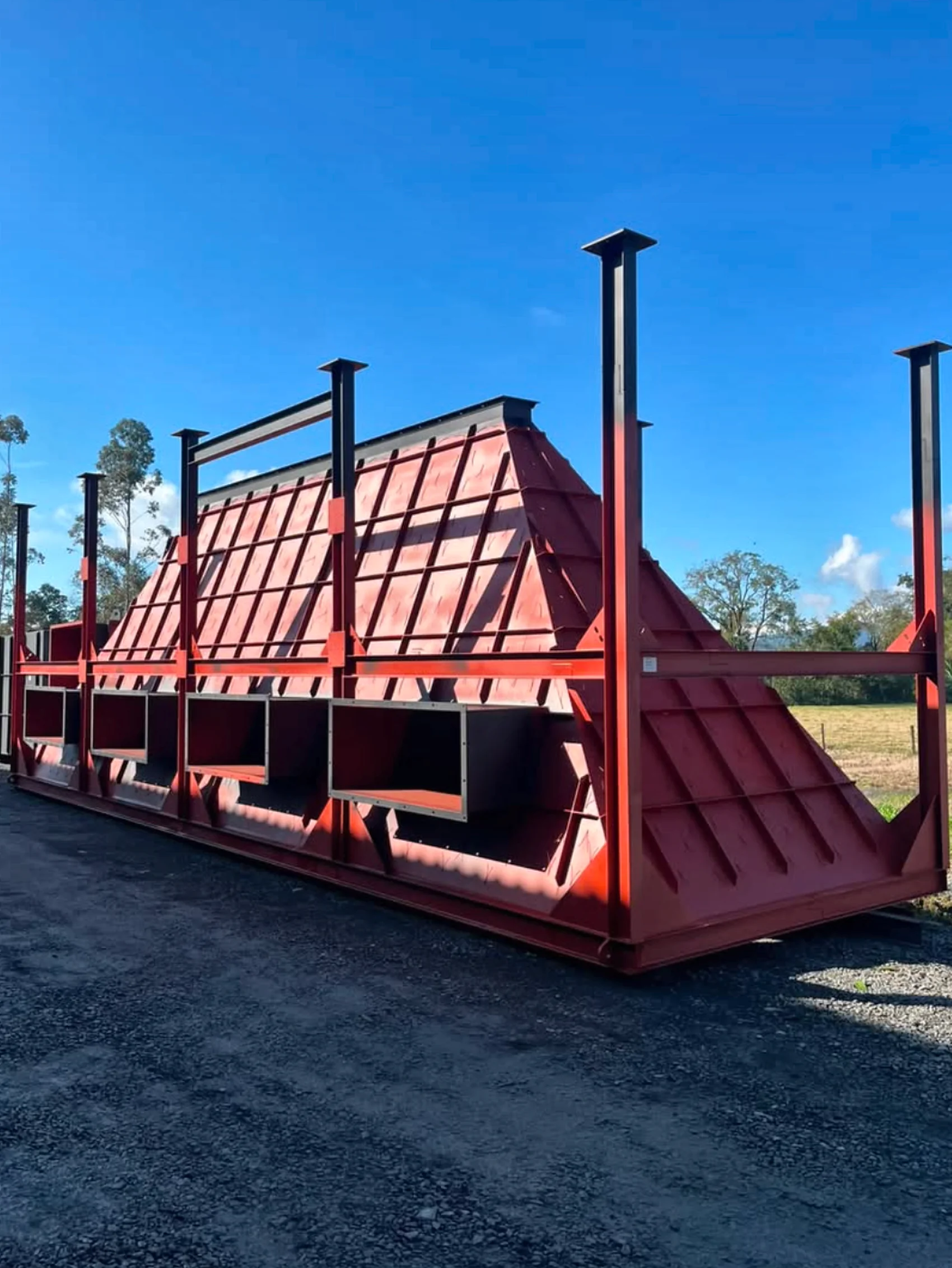 Grande equipamento industrial vermelho com estrutura metálica e reforços, fotografado no pátio da TOP1